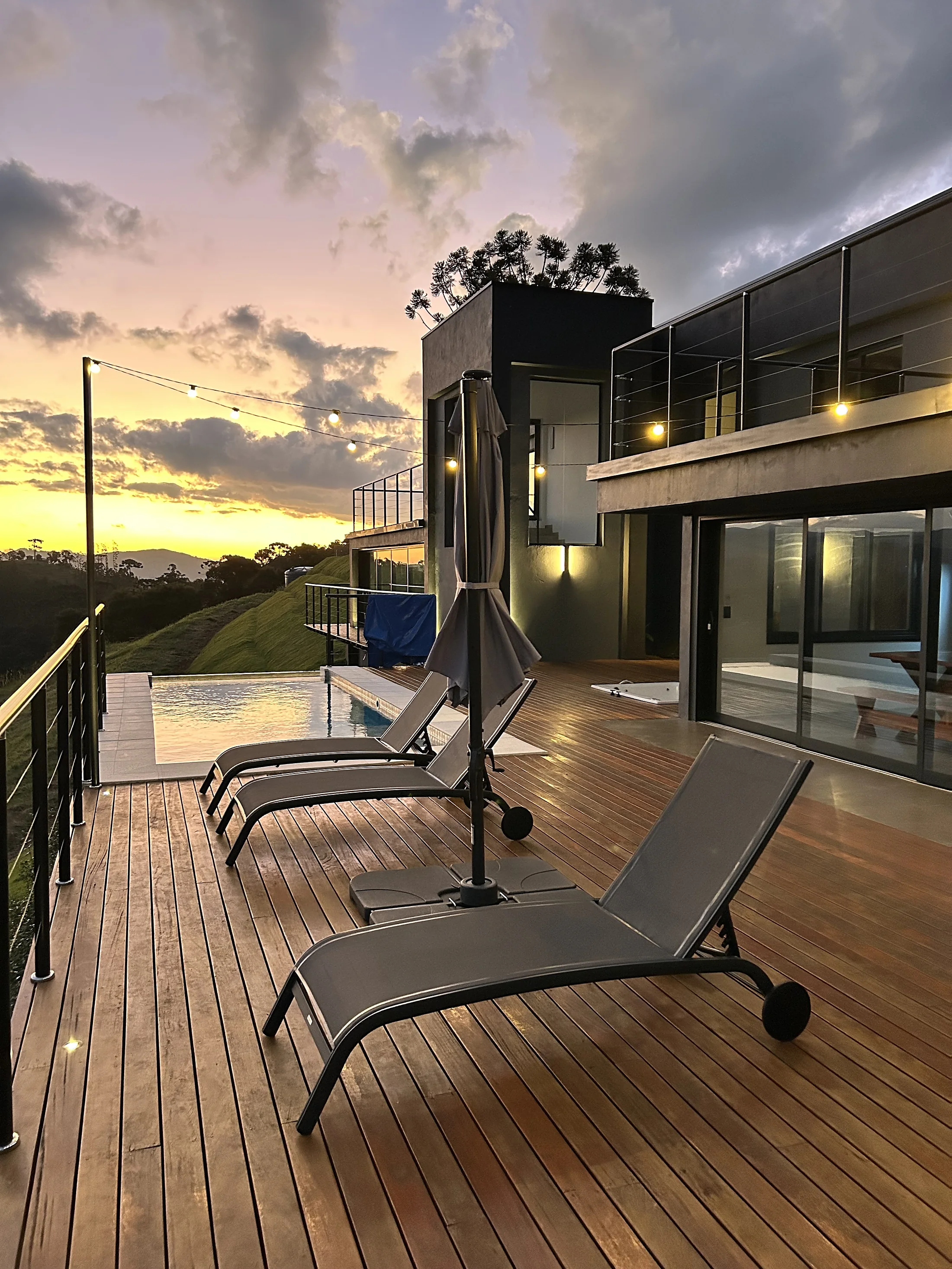 Deck com piscina de borda infinita e espreguiçadeiras ao pôr do sol dourado sobre a Serra da Mantiqueira
