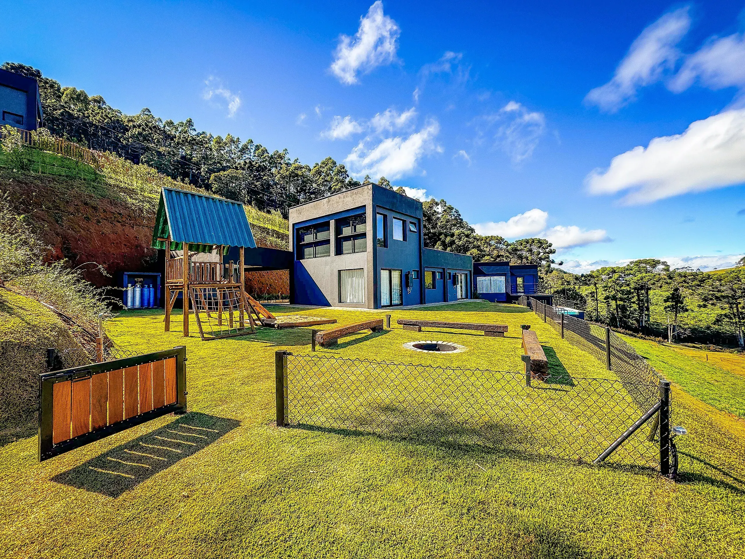 Fachada de arquitetura contemporânea em concreto grafite da Casa Mantiqueira, integrada ao gramado e às araucárias