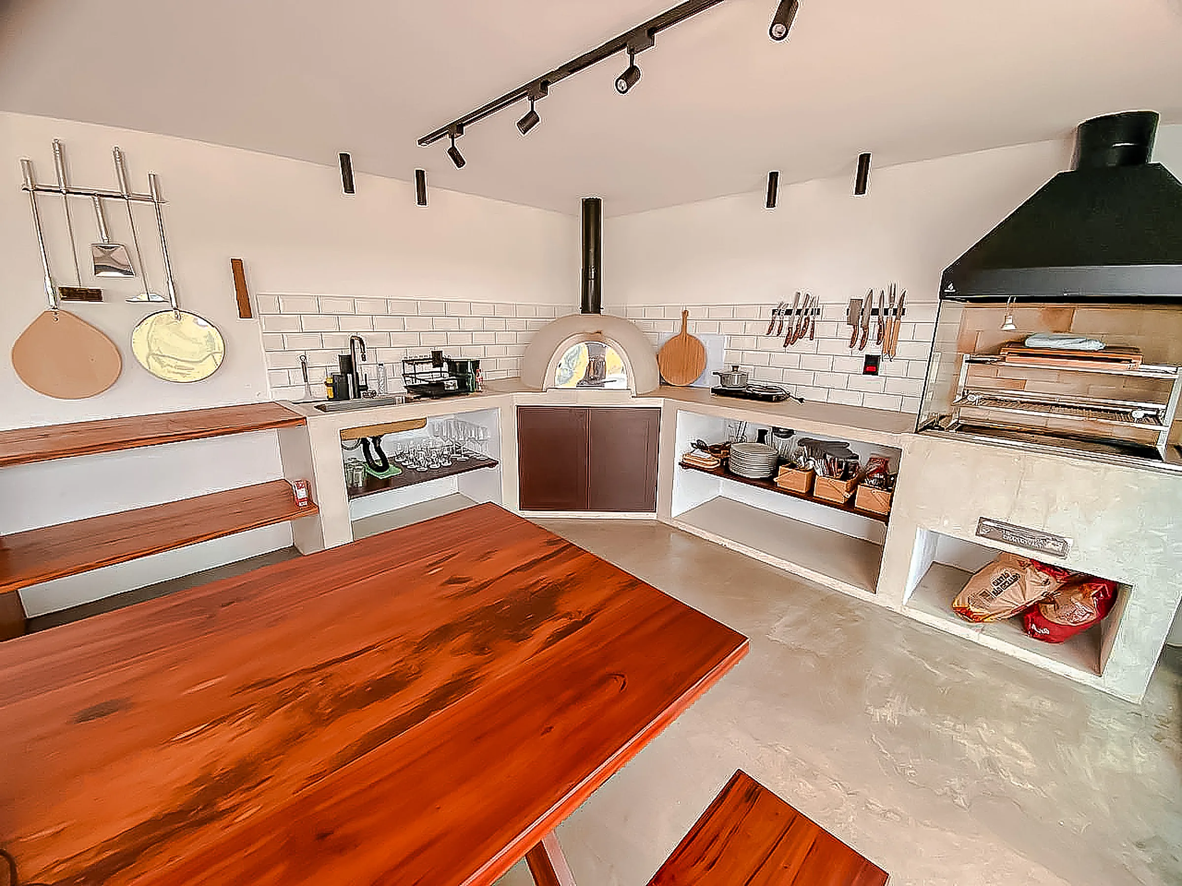 Área gourmet com forno a lenha e churrasqueira a carvão, bancada de concreto e mesa de madeira maciça