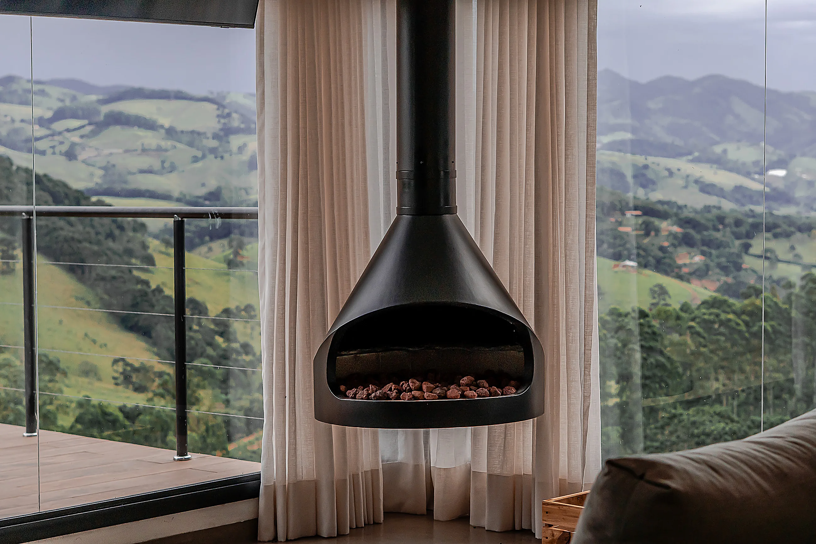 Living integrado com lareira suspensa, sofá e mesa de jantar de madeira diante de janelões com vista para os vales